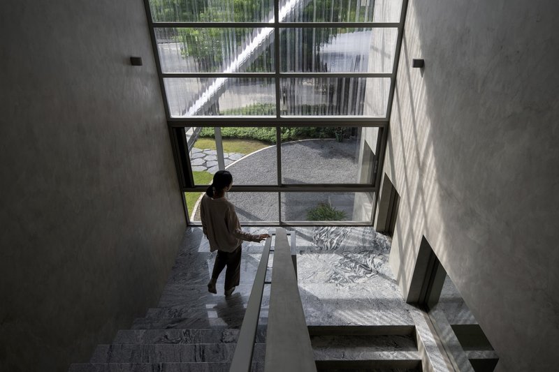 Top-down view of a person descending the staircase beside a full-height glazed wall overlooking the courtyard