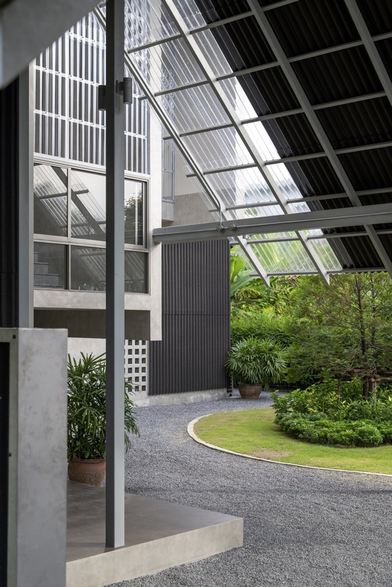 Covered entry courtyard with sloped glazed roof and gravel path winding through planted beds