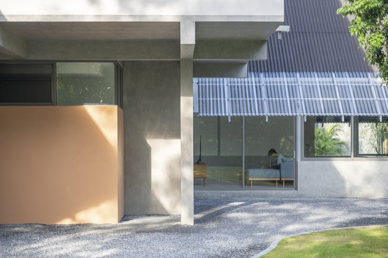 Covered concrete porch with peach-colored wall element and corrugated metal canopy in dappled sunlight
