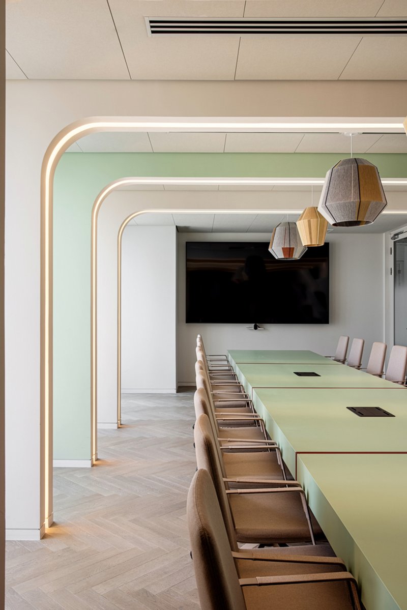 Conference room with rounded illuminated portal frames and a pale green table under pendant lights