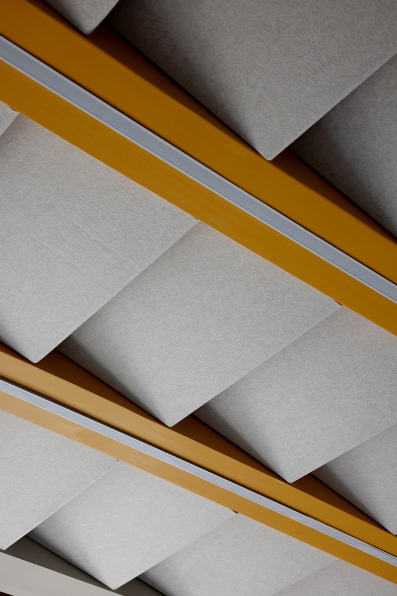 Ceiling detail showing white panels with yellow and tan timber beams casting angular shadows