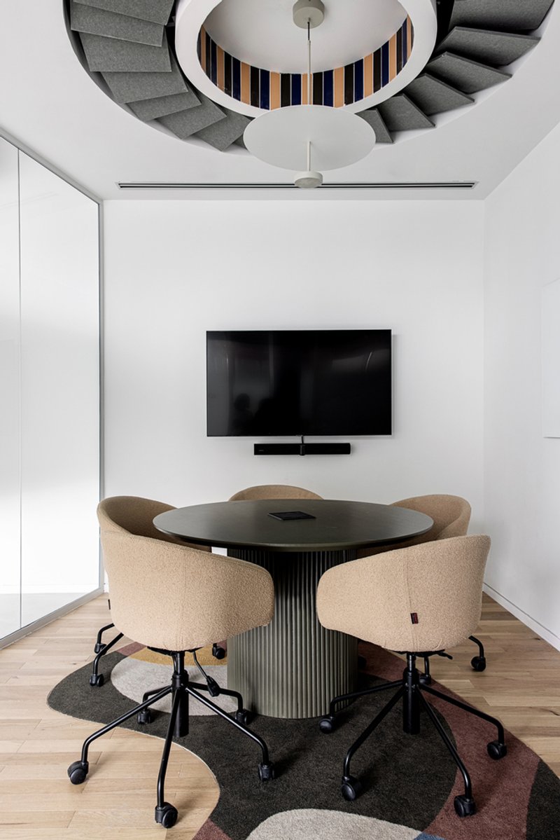 Small meeting room with circular opening revealing striped stairs and ceiling fan above