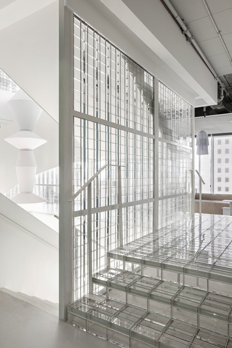 Glass block staircase ascending alongside a gridded translucent screen wall with white railing