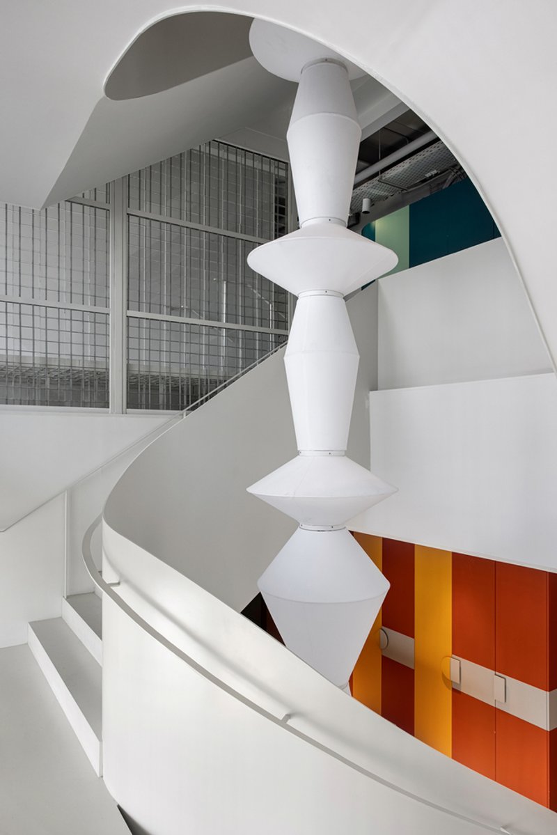 Atrium view of the curved balconies and white sculptural column with translucent mesh screen partitions and colored panels below