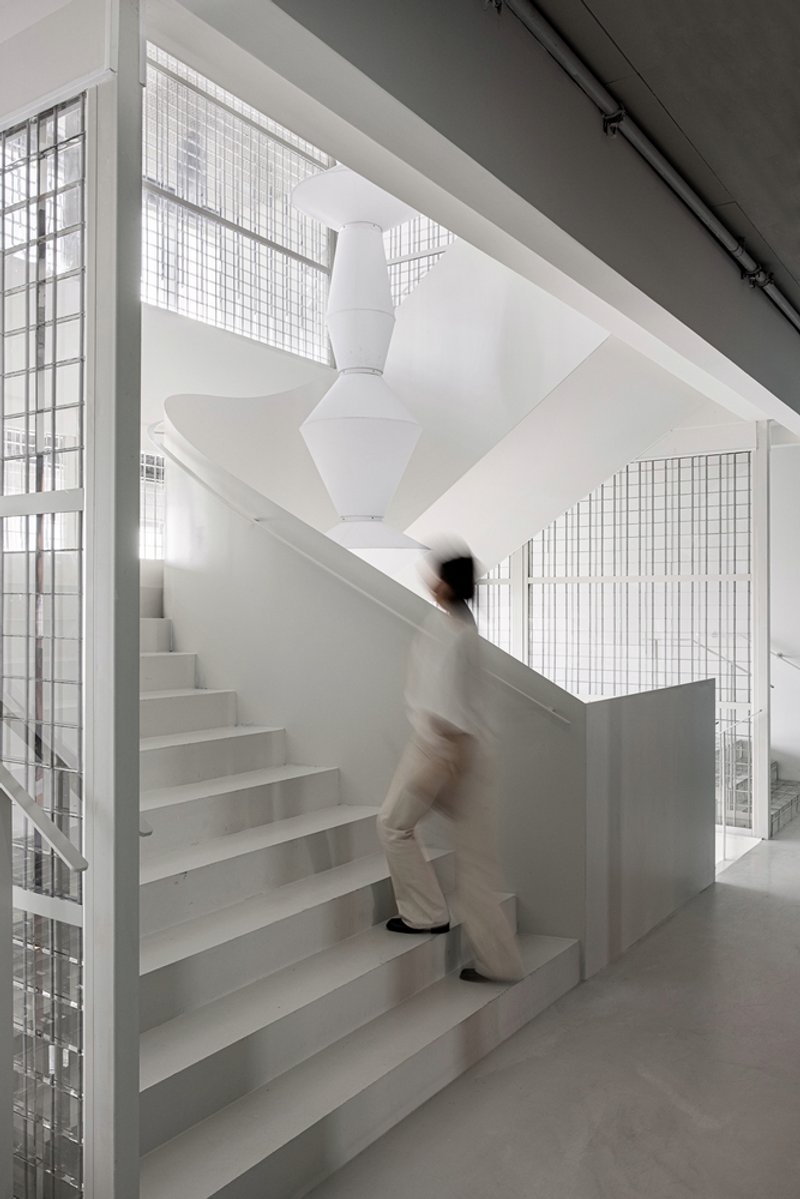 Central staircase with a figure in motion ascending the steps behind wire mesh partitions and white sculptural column overhead