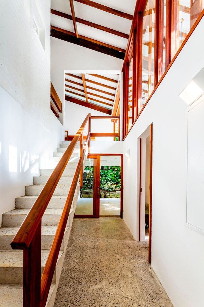 Stairwell with timber railings and terrazzo treads beneath exposed timber roof structure and clerestory glazing