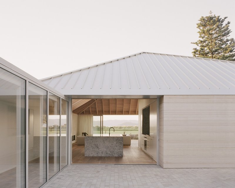 Covered terrace with standing seam metal roof framing a view into the open kitchen with stone island