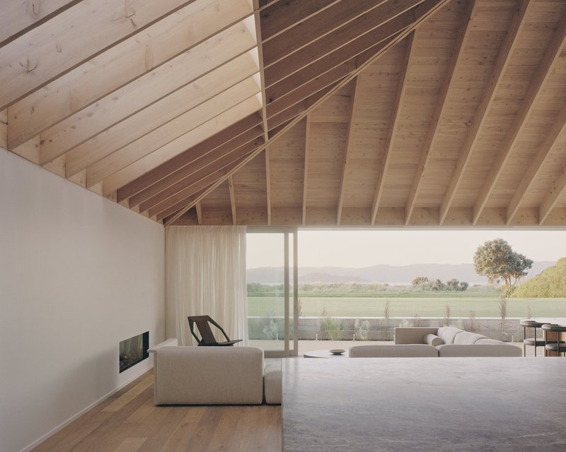 Living room with exposed timber rafters and full-height glazing opening to a terrace overlooking rural fields