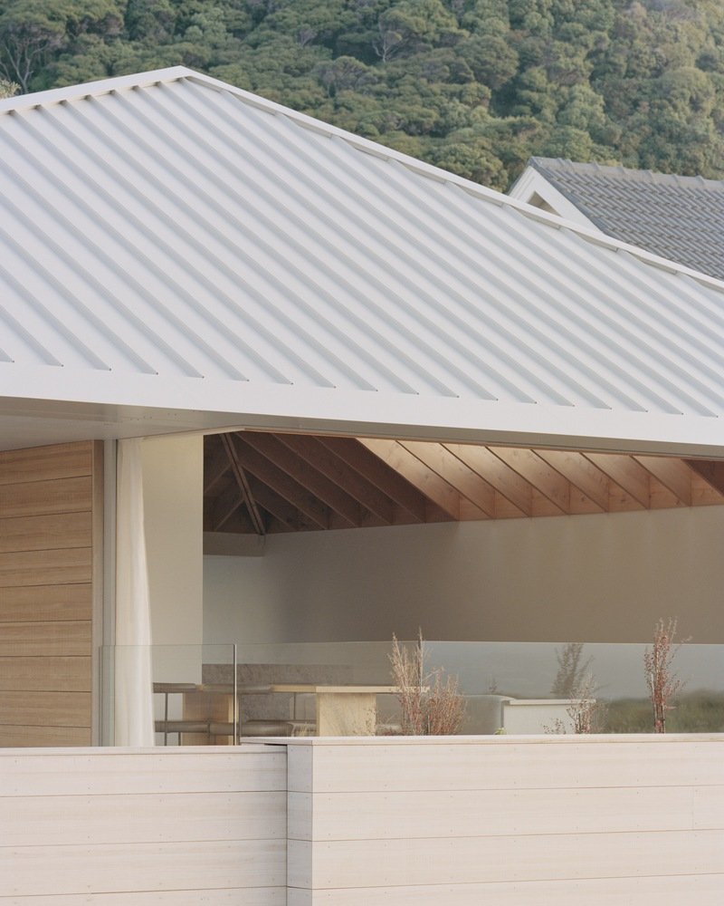 Detail of the metal-clad gable roof meeting horizontal timber cladding with hillside vegetation beyond