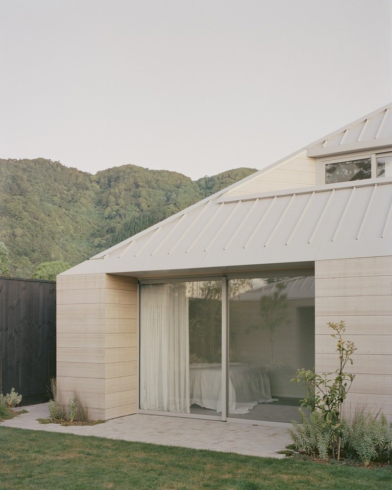 Bedroom pavilion with angled metal roof and sliding glass door opening to a lawn at dusk
