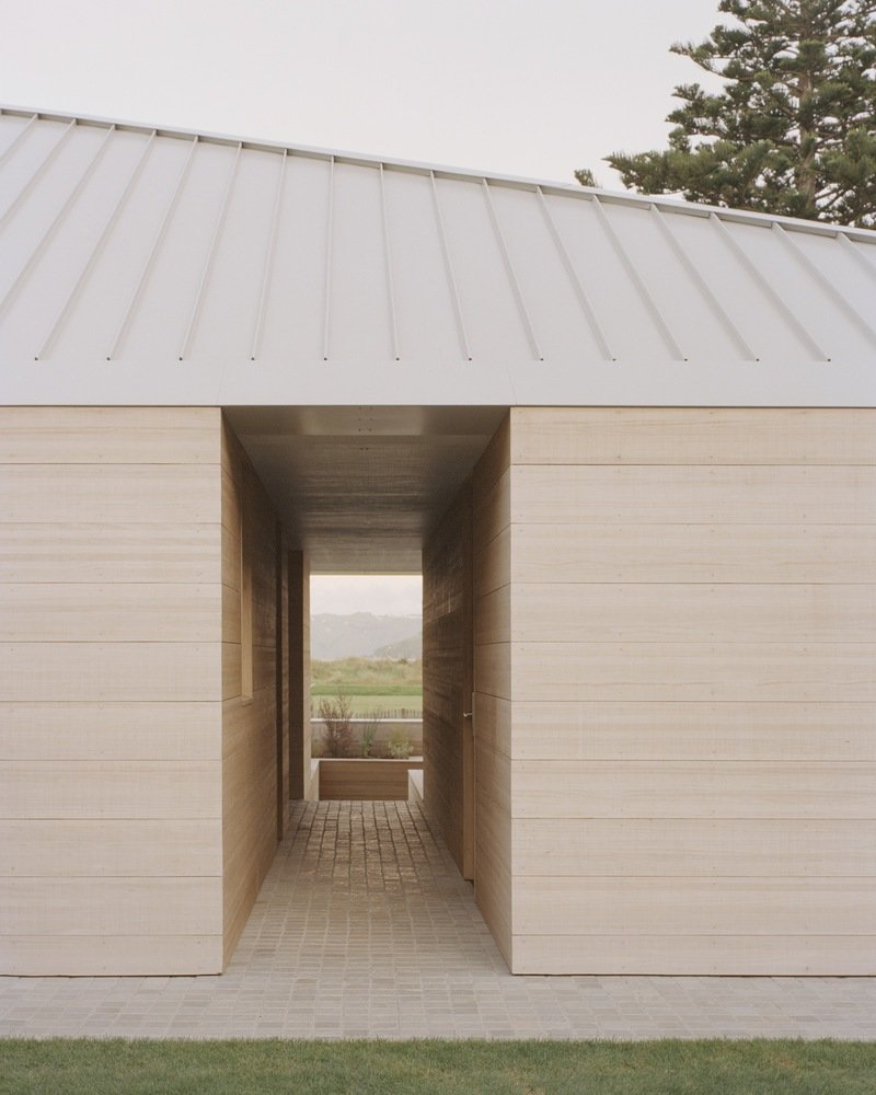 Covered passage through horizontal timber cladding with paved brick floor and view to distant landscape