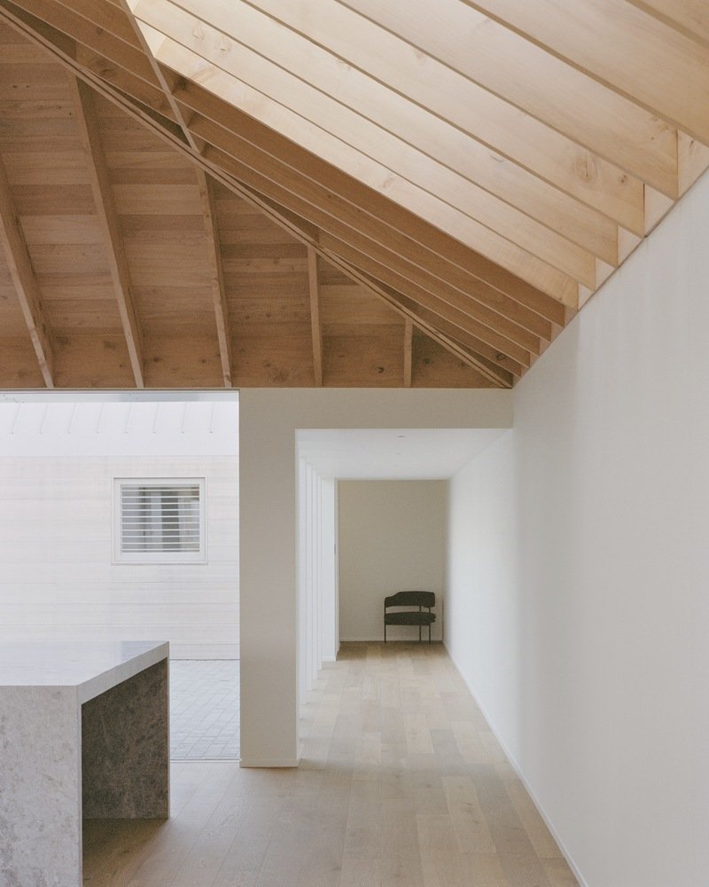Interior corridor with exposed timber ceiling joists and stone flooring leading to a distant chair