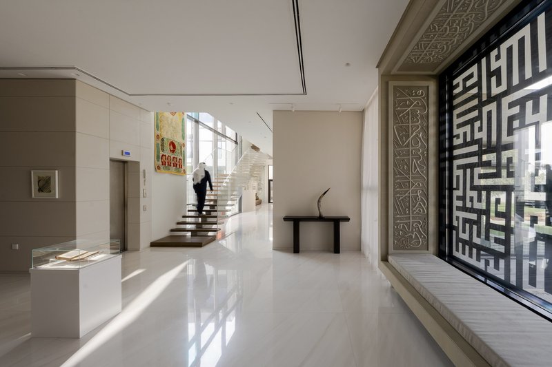 Entrance hall with floating timber staircase and geometric perforated screen filtering afternoon light
