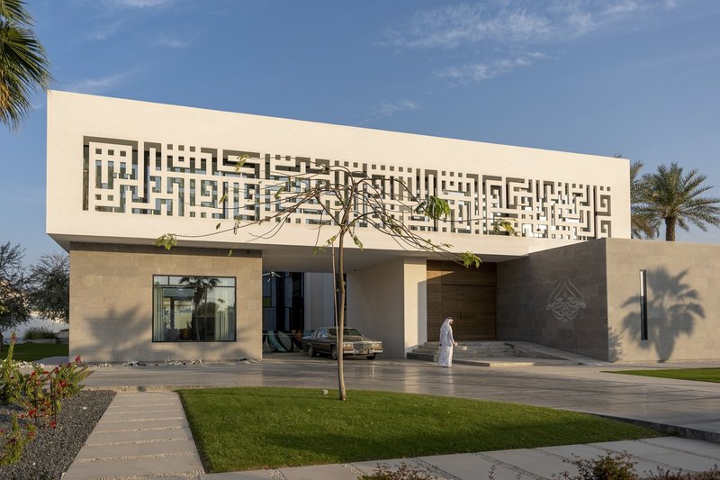 Front facade showing perforated white upper volume above concrete plinth with figure in white robe