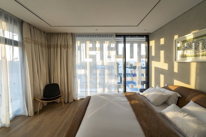 Bedroom with sheer curtains casting geometric screen shadows onto the wall at midday