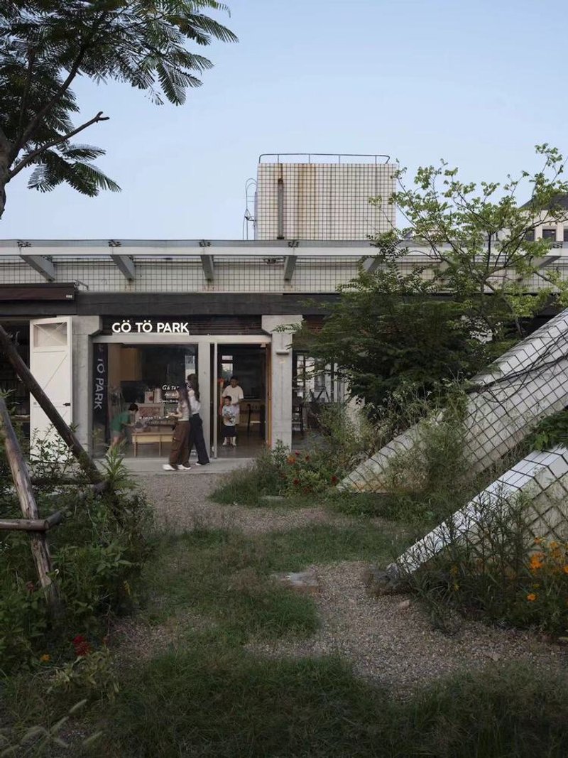 Gravel pathway through planted landscape leading to glazed shopfront beneath white tiled rooftop structure