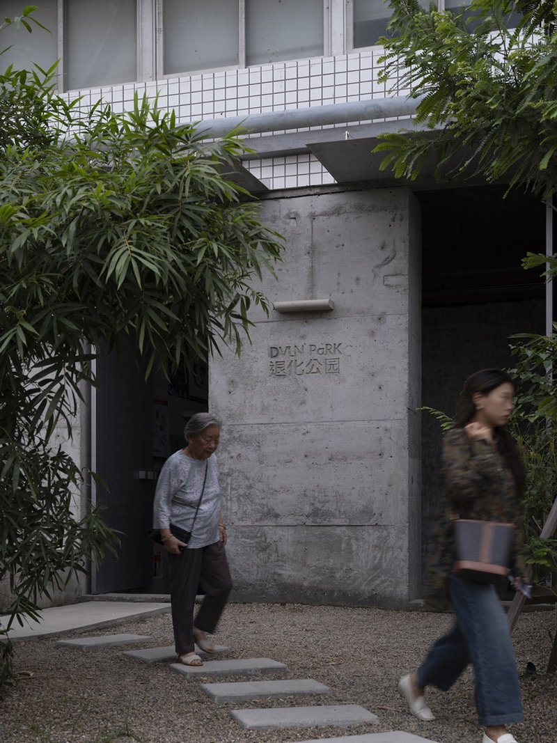 Concrete entrance wall with carved signage flanked by bamboo plantings and stepping stones as visitors pass