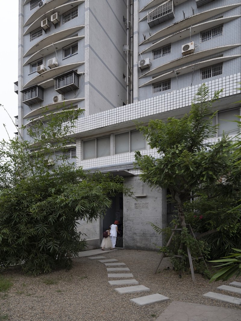 Stepping stone path through planted garden leading to concrete doorway beneath white tiled residential facade