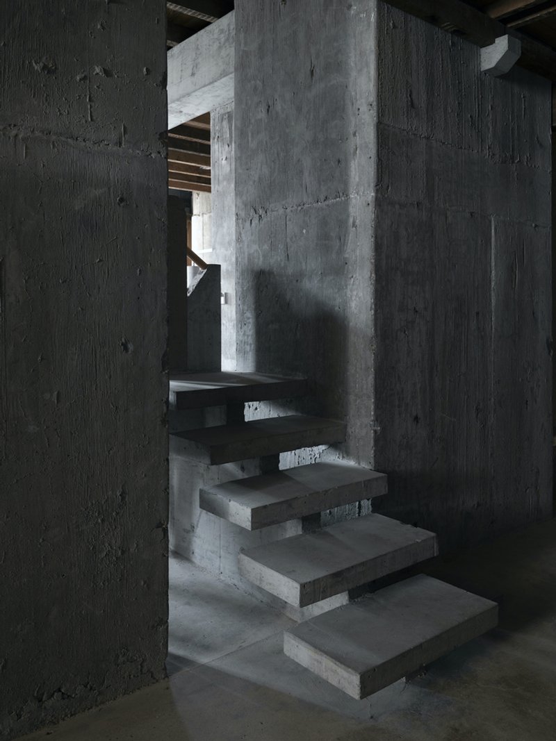 Floating concrete staircase with open risers between exposed concrete walls and columns