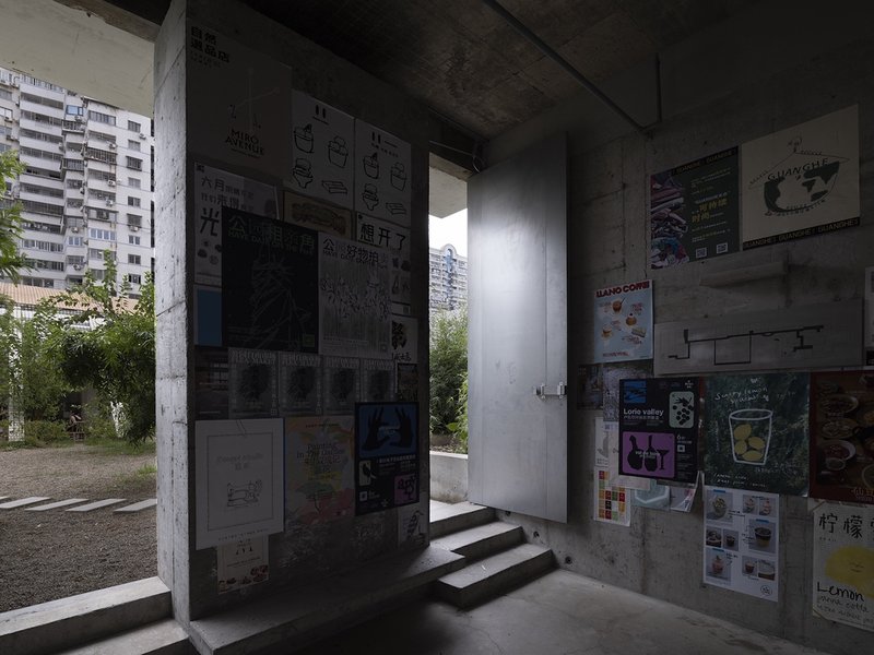Concrete doorway with steps opening to planted garden framed by poster-covered walls