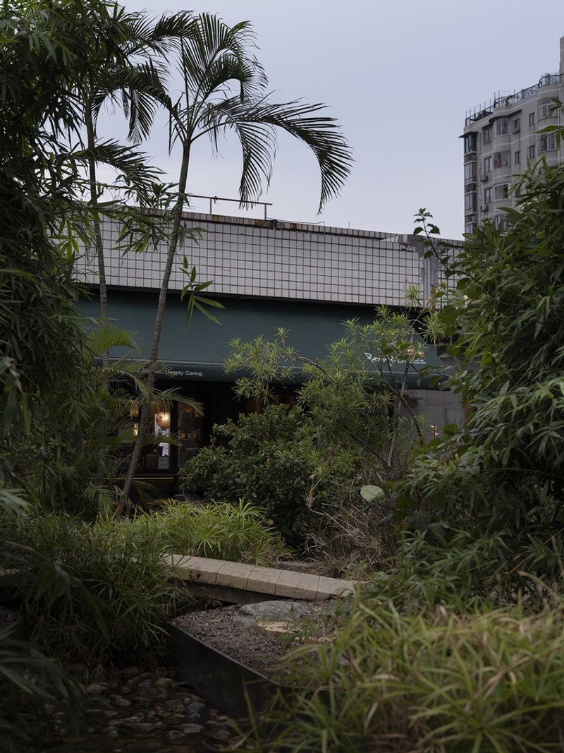 White tiled bridge volume crossing planted courtyard with palm trees at dusk