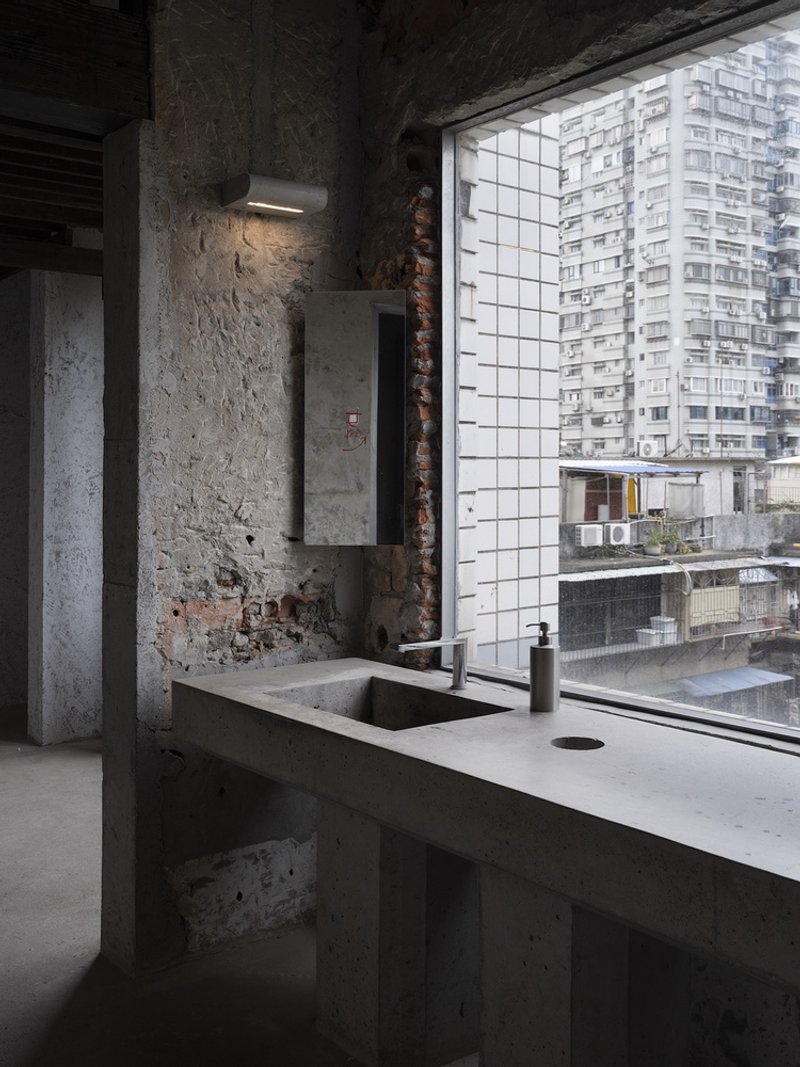 Concrete kitchen counter with sink beside exposed brick wall and gridded window overlooking residential towers