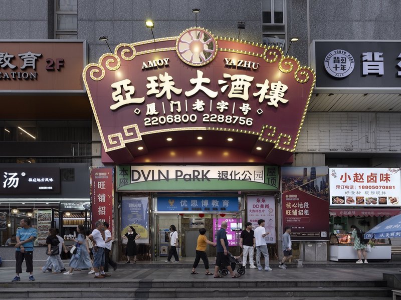 Street-level storefront with illuminated signage and pedestrians passing at dusk