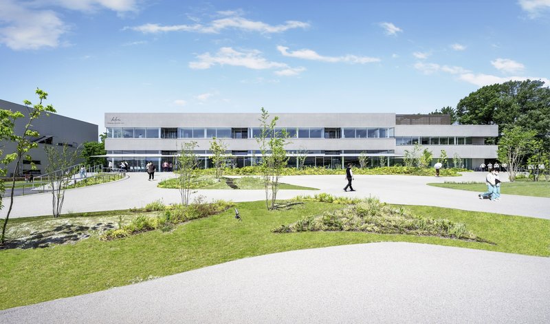 Front facade with horizontal window bands and landscaped courtyard with planted beds and pathways under blue sky