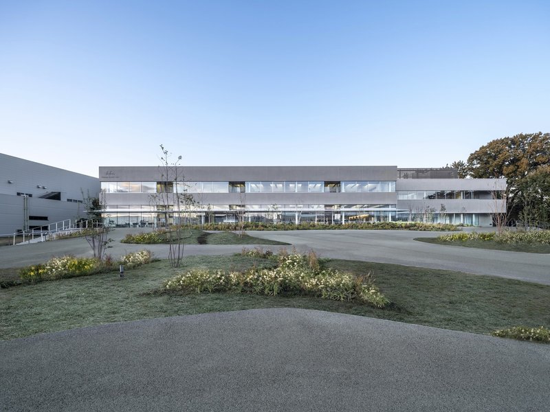 Horizontal facade with continuous window bands viewed across landscaped forecourt with curving pathways at dusk