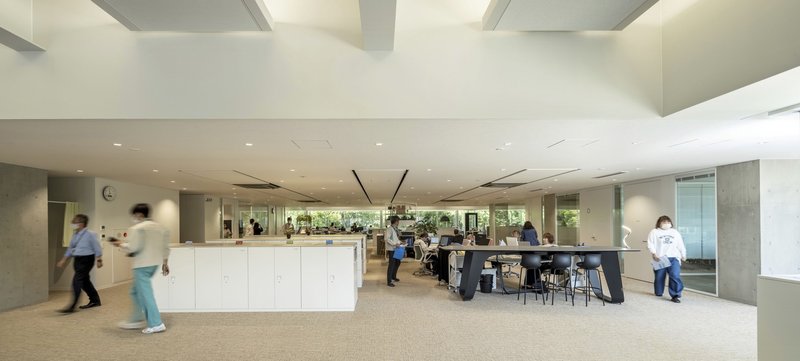 Office breakout area with white storage islands, exposed concrete columns, and staff moving through the carpeted central circulation zone