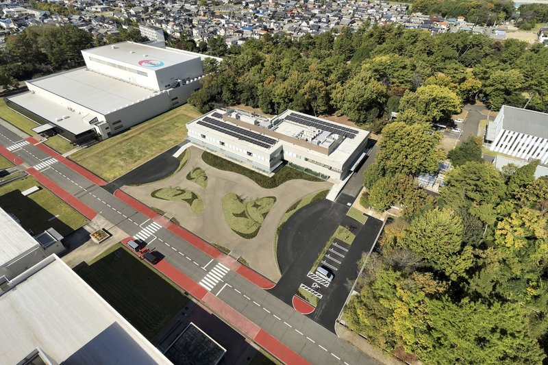 Aerial view of the white-roofed building surrounded by sculpted landscape mounds and mature tree canopy