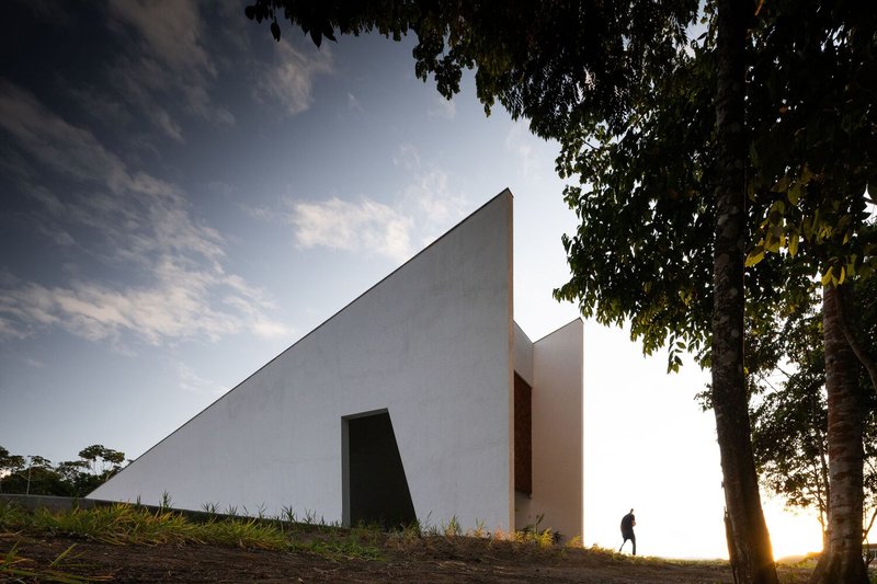 Sloping white wall with recessed opening at golden hour with figure walking in backlit grass