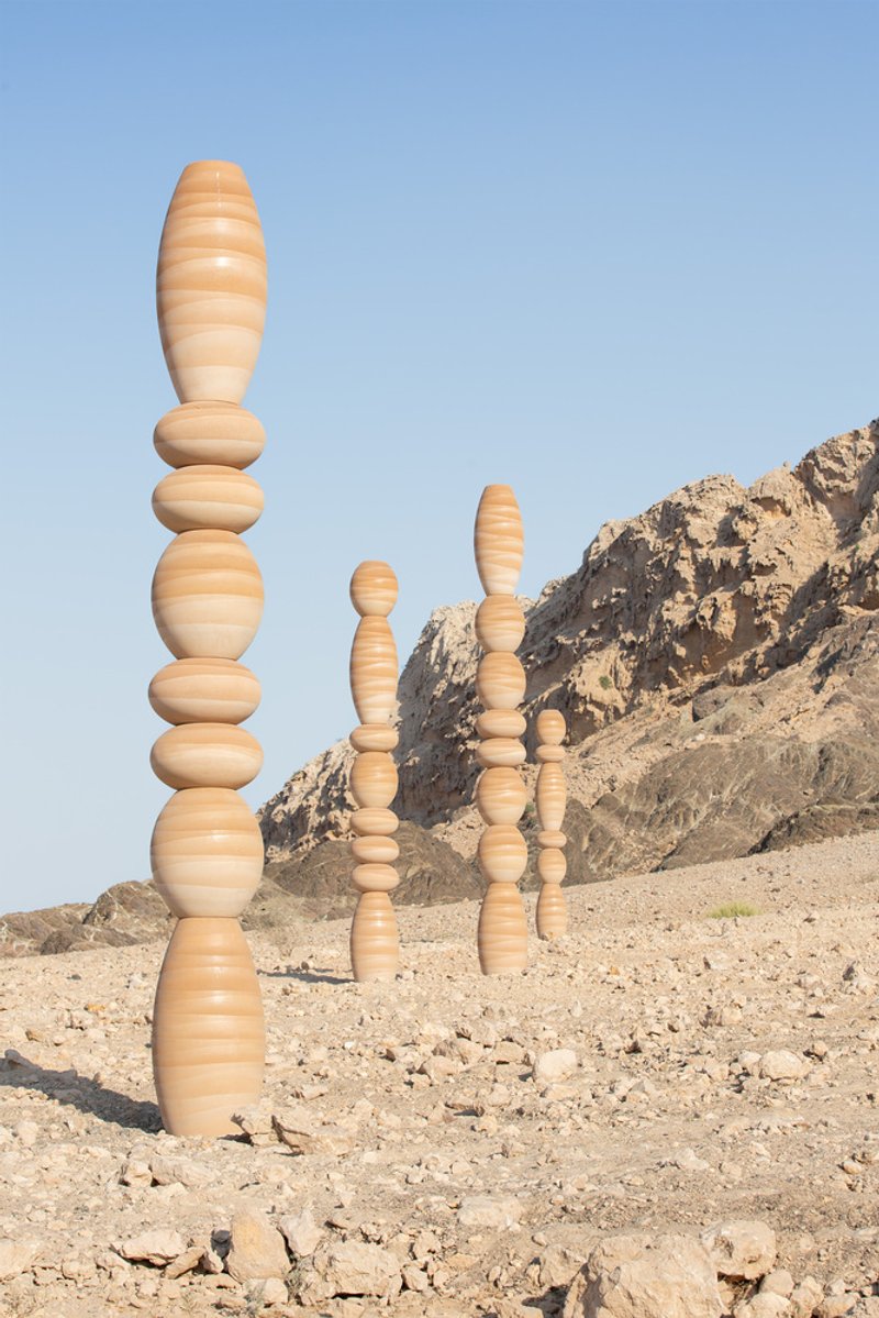 Cluster of laminated wood columns with alternating light and dark grain against a rocky hillside