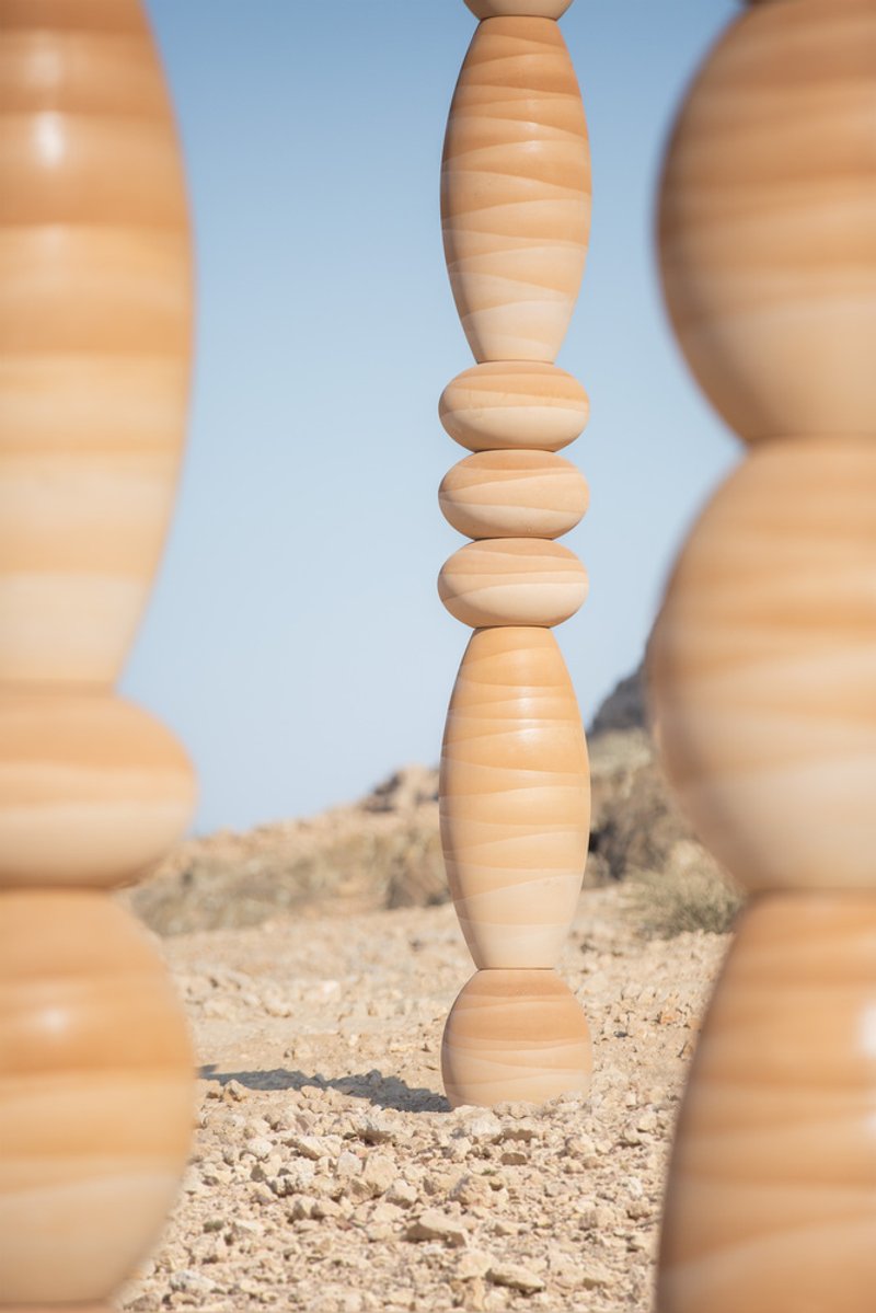 Close view through foreground columns showing the stacked spherical and elliptical segments of a central timber piece