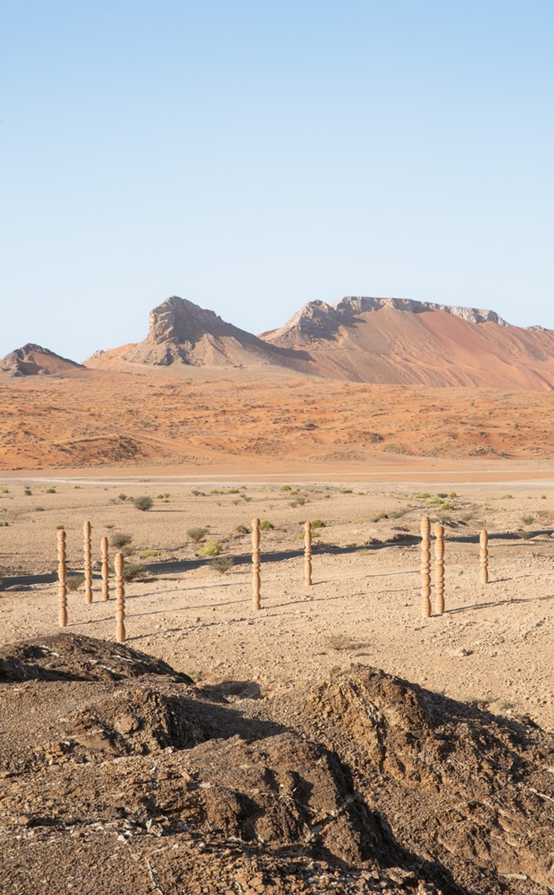 Grouped timber columns with bulbous segments anchored in the sandy ground beneath a clear sky