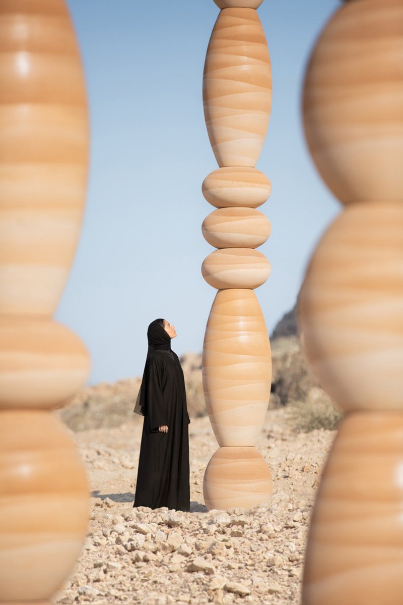 Figure in black robes framed between stacked wood columns with elliptical and spherical segments