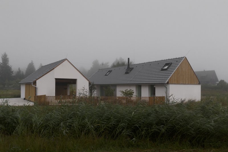 Cluster of gabled volumes with white render and timber cladding across a grassy field in dense fog