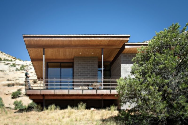 Elevated timber and concrete block residence with horizontal railing deck overlooking a sloping desert hillside