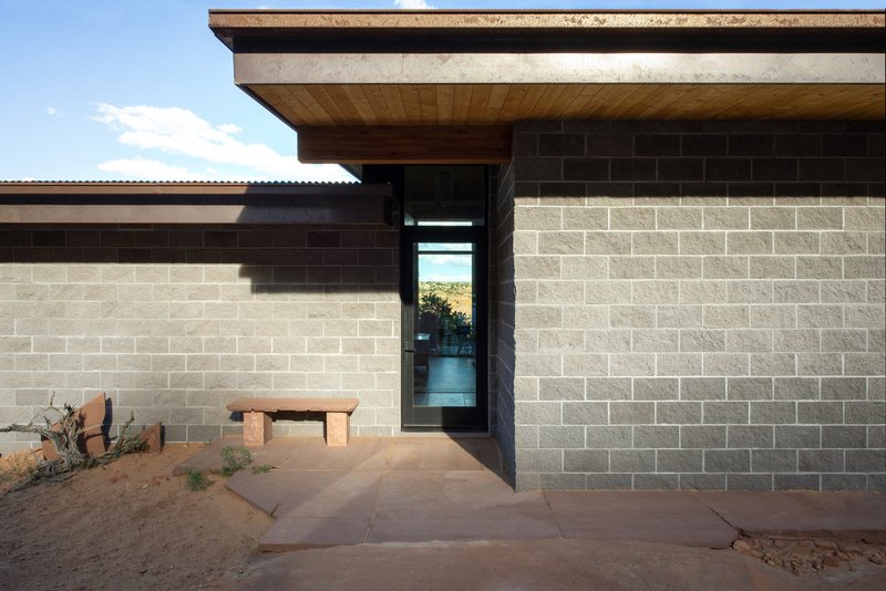 Entry facade with two-tone concrete block walls and narrow glazed slot opening beside timber soffit overhang