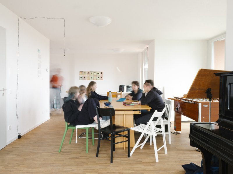 Open living space with family gathered around a wooden dining table near a piano