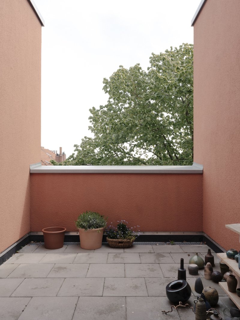 Private terrace with terracotta walls and potted plants framed by a mature tree beyond