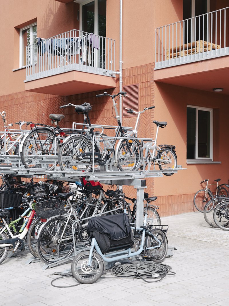 Two-tier bicycle parking racks filled with bikes beneath residential balconies with white railings