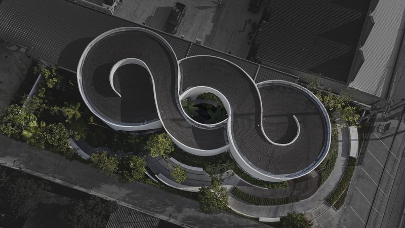 Aerial view of three spiral-shaped roof volumes with planted courtyards and paving between neighboring buildings