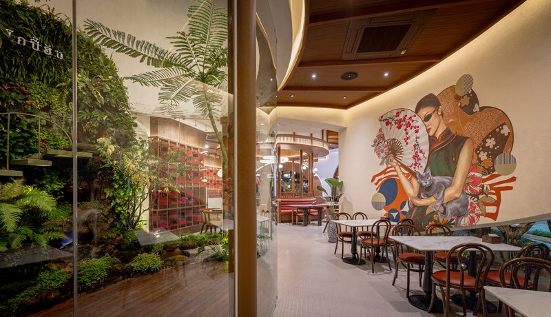 Dining space with glass-enclosed planted courtyard and wall mural of figures in traditional dress