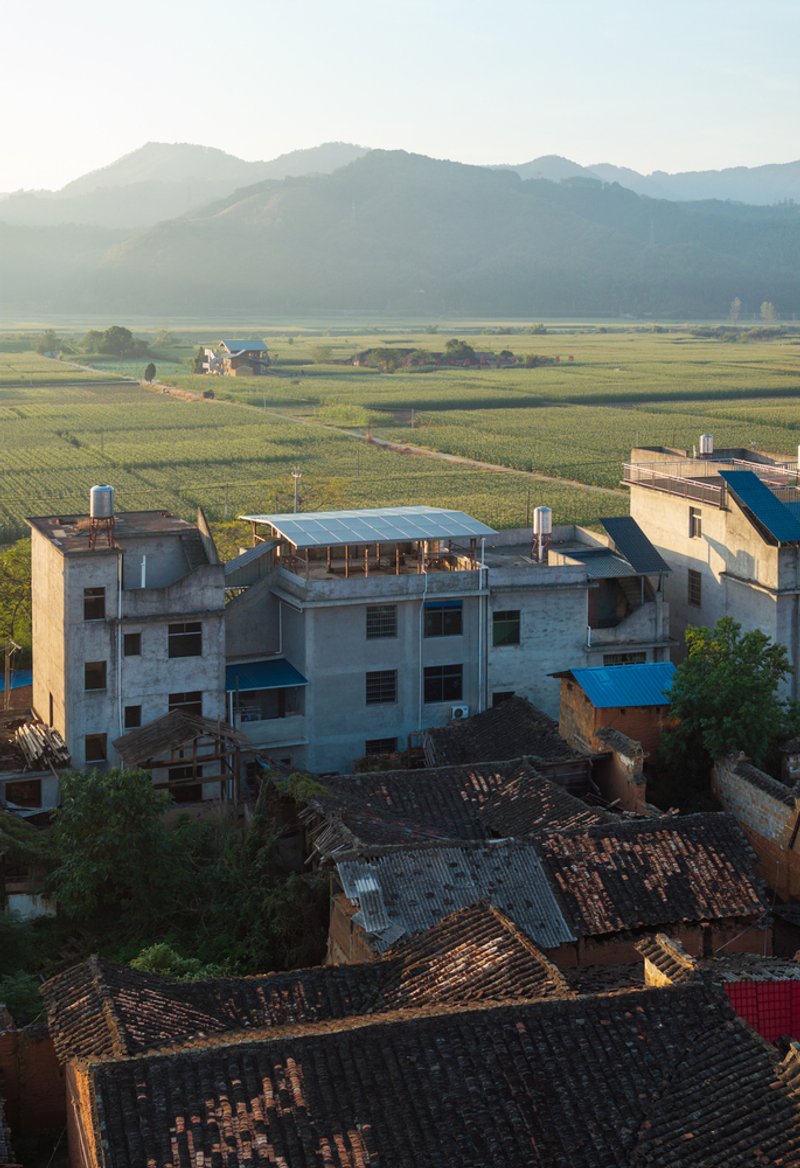 Aerial view of concrete and brick village rooftops with mountains and agricultural fields in morning mist