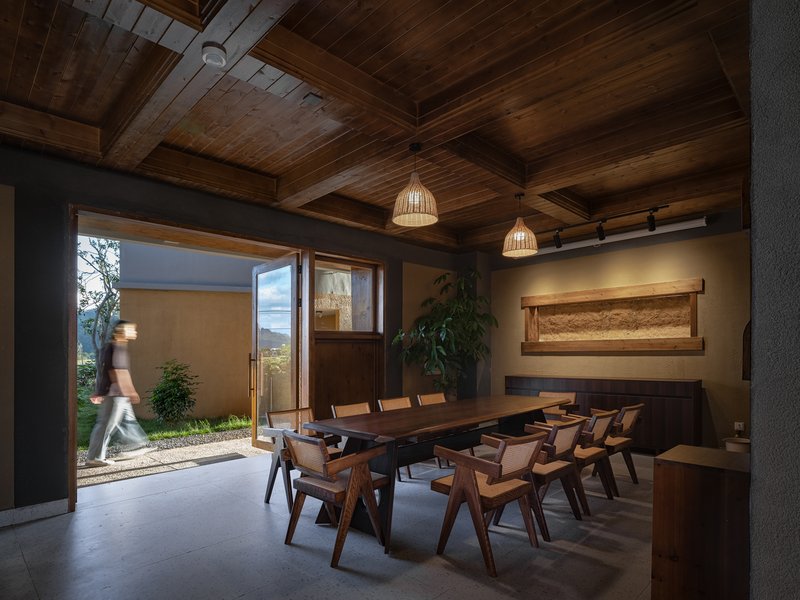 Dining room with exposed timber ceiling and open doors leading to a courtyard with a figure passing through