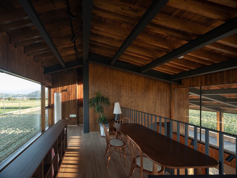 Dining space with exposed timber ceiling beams and metal railings overlooking the landscape through full-height glazing