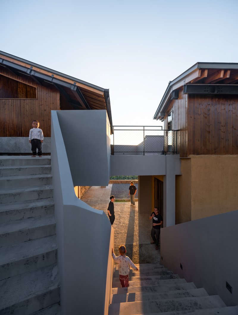 Outdoor staircase connecting split-level terraces between timber volumes with children playing at dusk