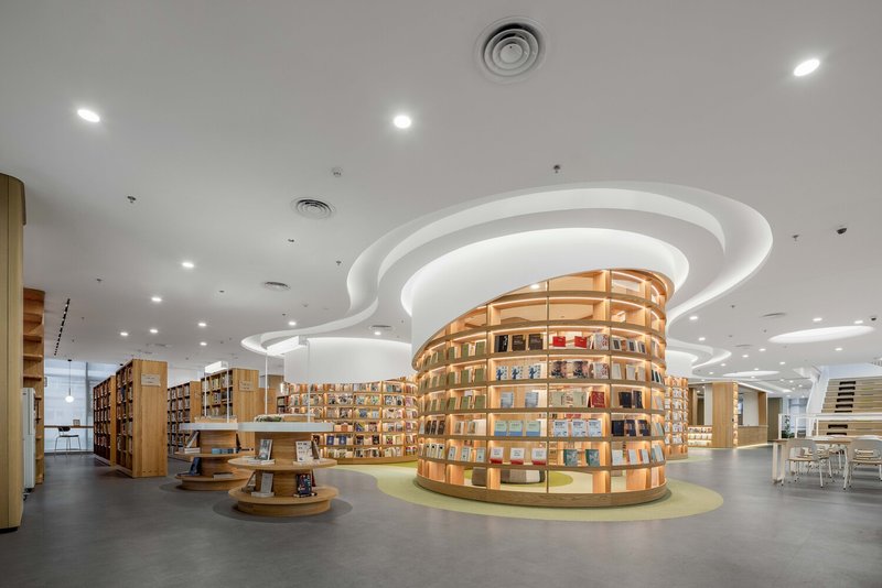 Interior library space with circular wood bookshelves under swirling white ceiling planes with integrated lighting