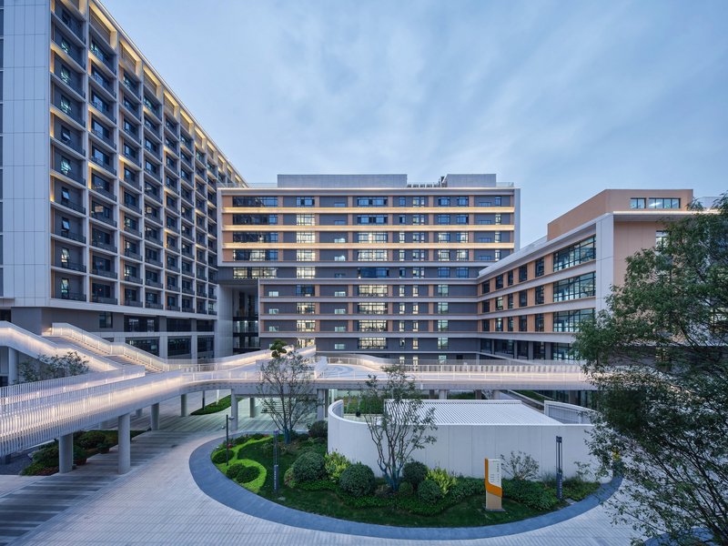 Residential courtyard with curved landscaped beds and an illuminated pedestrian bridge at twilight